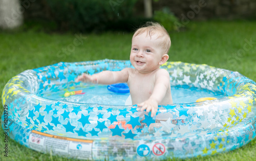 Cute 9 months old baby boy having fun in inflatable swimming pool