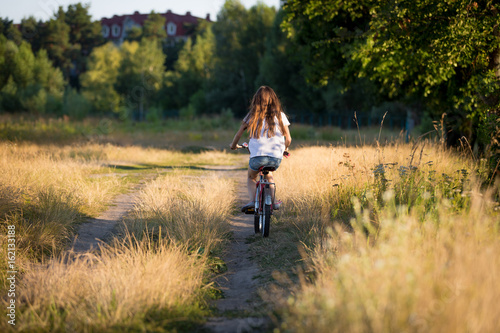 Beautiful girl riding bike at fields at sunset