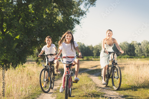 Family riding on bicycles in meadow at sunny day