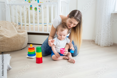 Young mother playing and teaching her baby boy on floor at living room