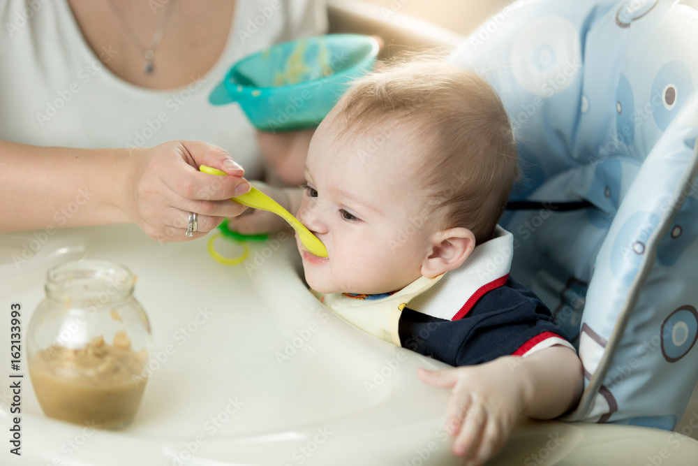 Young mother feeding her baby in highchair Young mother feeding her baby in highchair