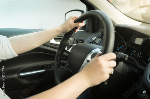 Young woman driving car and holding hands on steering wheel