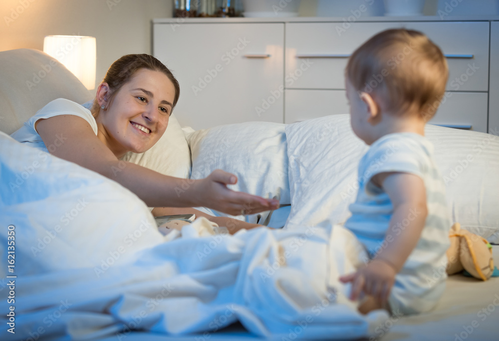 Beautiful smiling woman with baby in bed at night