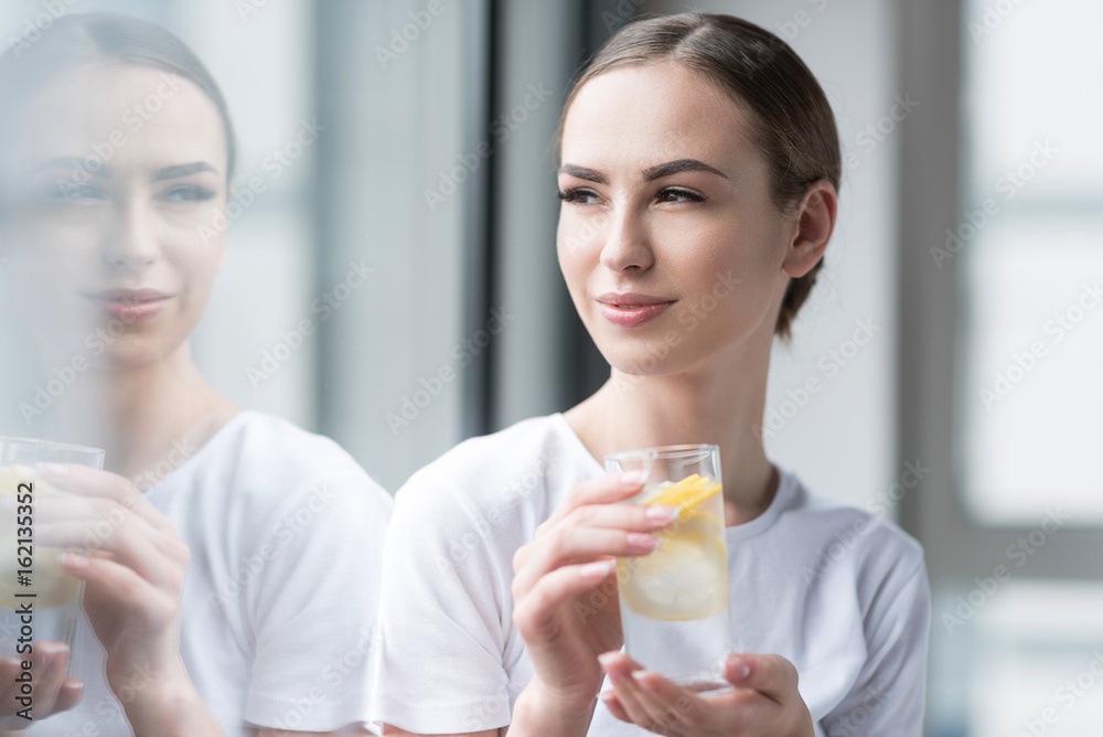Happy attractive girl drinking water with fresh lemon indoors Happy attractive girl drinking water with fresh lemon indoors