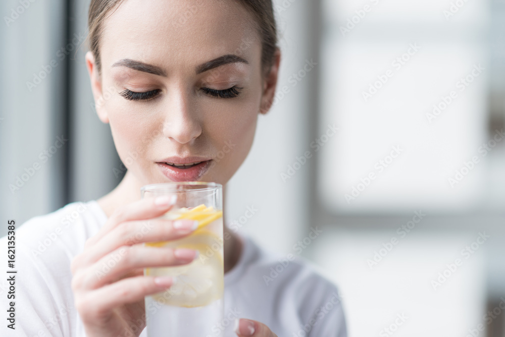 Calm beautiful girl with perfect make-up drinking fresh lemon water Calm beautiful girl with perfect make-up drinking fresh lemon water