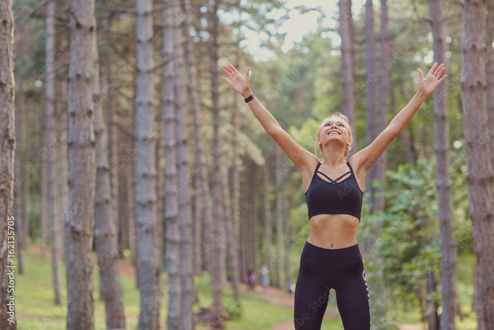 The sports girl raised her hands in the forest. Concept of victory motivation in sports.