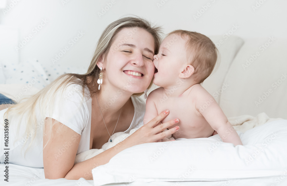 Portrait of cheerful mother hugging and kissing her baby boy on bed Portrait of cheerful mother hugging and kissing her baby boy on bed