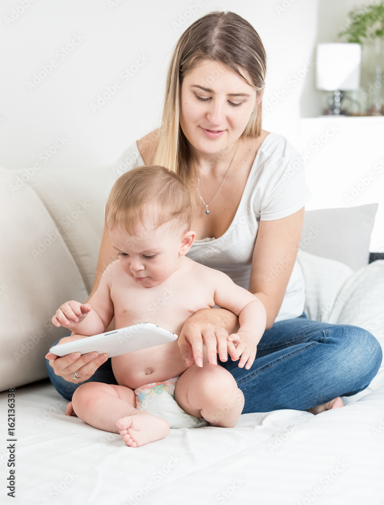 Concentrated baby boy and young mother touching screen on tablet PC Concentrated baby boy and young mother touching screen on tablet PC