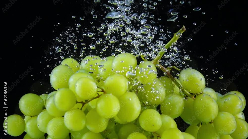 Two clusters of juicy green grape dropping into the water in slow motion. Shooting with high-speed camera.
