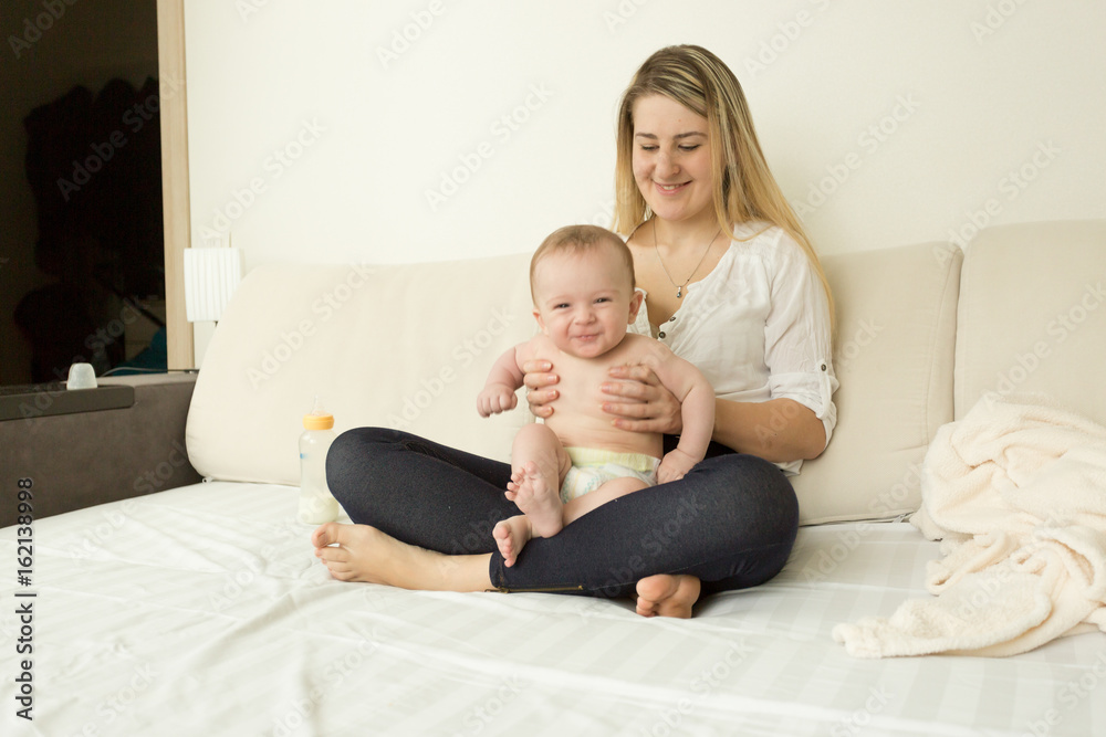 Smiling young mother sitting on bed with her baby boy Smiling young mother sitting on bed with her baby boy
