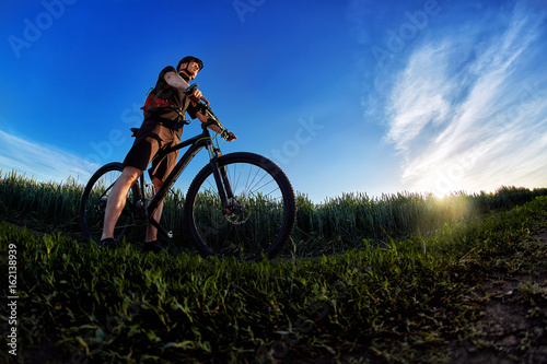 Wide angle of the cyclist standing on the trail on the field against beautiful landscape.