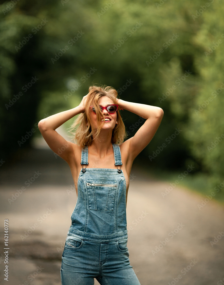 Young woman in denim overalls on forest road.