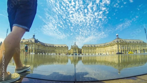 People enjoy sunny summer day near water mirror fountain on Place de la Bourse in Bordeaux, Nouvelle-Aquitaine region, France. One of the most popular attractions in Bordeaux. 4K UltraHD