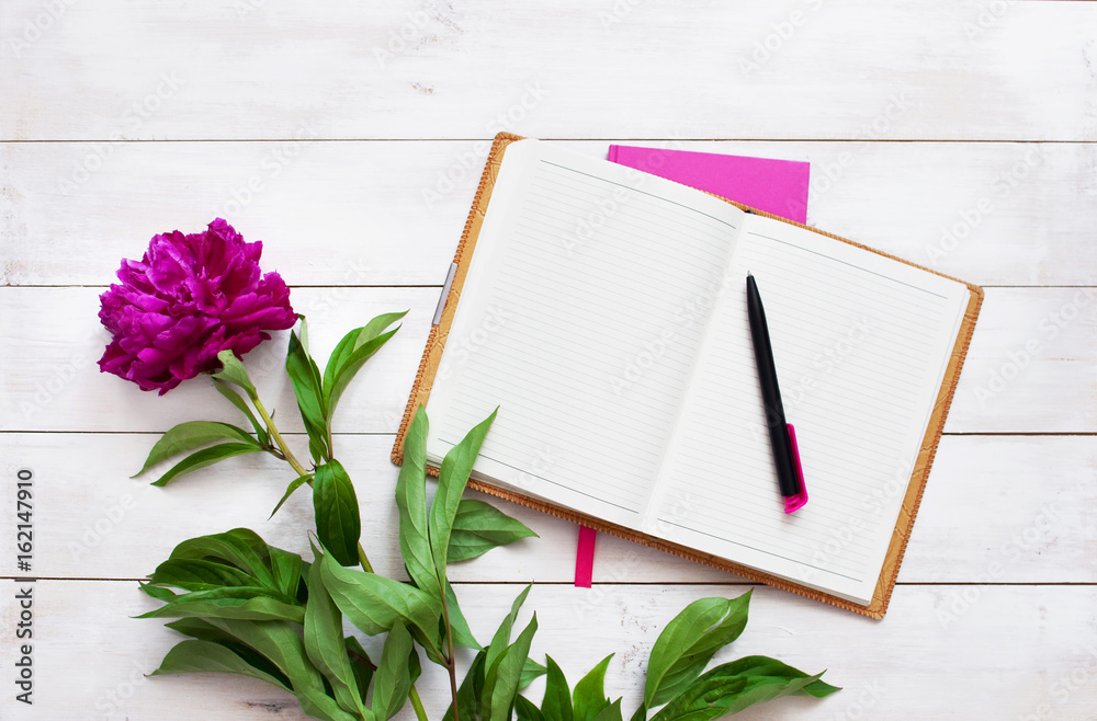 Naklejka premium Notepad, pen and flowers of peonies on white table. Female objects for work top view with copy space.