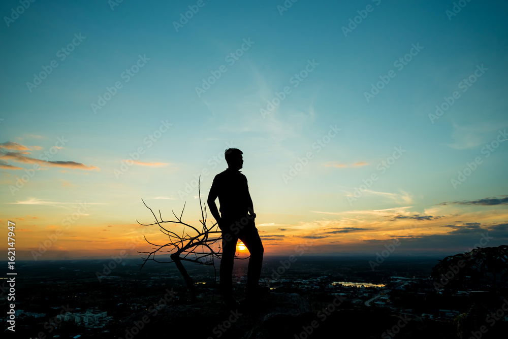 Silhouette of young man on sunset or sunrise. Confident teenage boy thinking. Hope. Sadness. Freedom.