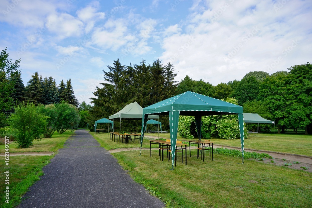 Green garden tent, garden pavilion. Rest area with  chair and picnic tables and green tent installed on green lawn in a park
