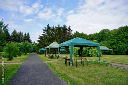 Green garden tent, garden pavilion. Rest area with chair and picnic tables and green tent installed on green lawn in a park 
