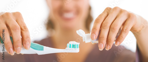 Closeup on happy young woman squeezing toothpaste from tube