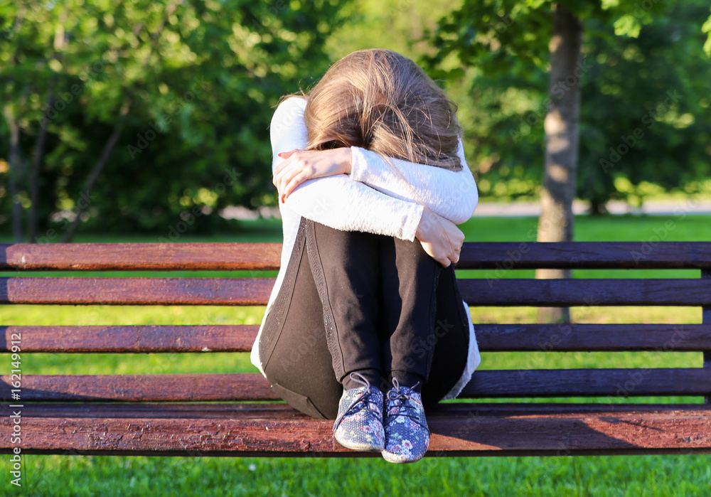 Sad girl sitting on a bench Stock Photo | Adobe Stock