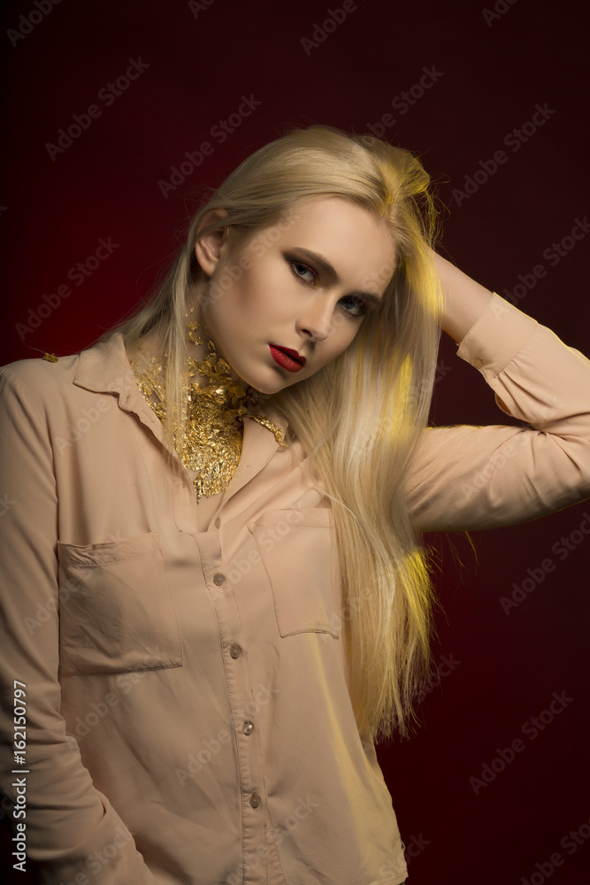 Stunning young model with perfect makeup in red color and gold foil on her neck