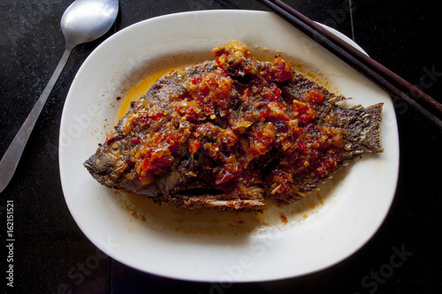 Fish topped with chili food of Thailand on Black tile.with Chopsticks and spoon.