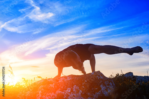 Attractive man doing yoga on the rock in the morning against sunrise.