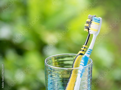 Duo Toothbrushes in glass on blurred green background