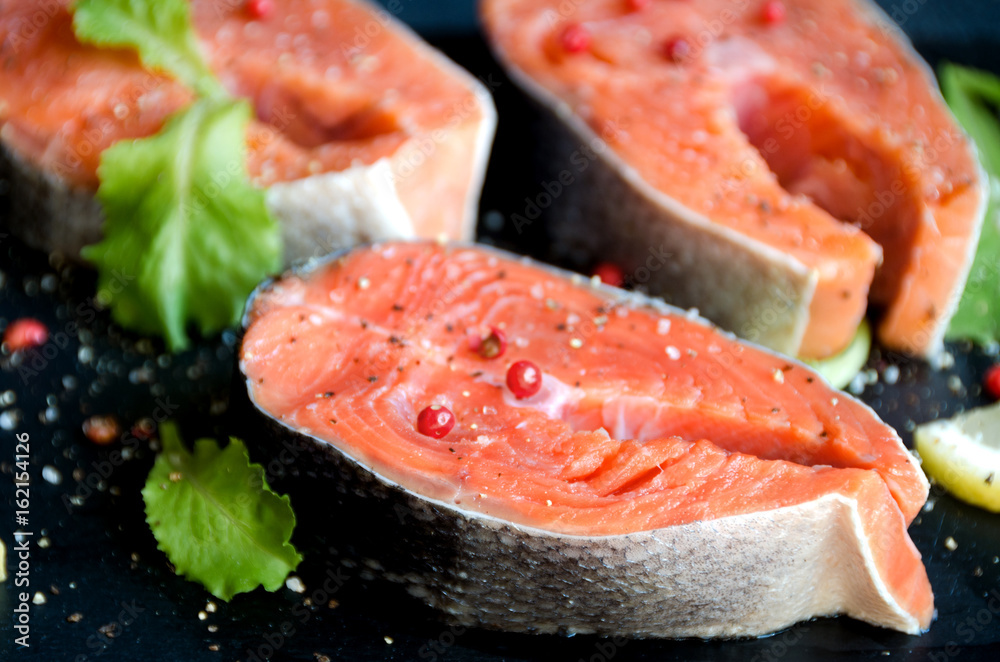 Salmon steaks pepper salt greens black plate Salmon steaks pepper salt greens black plate
