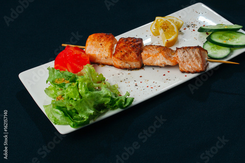 Shashlik of salmon with vegetables on white plate and black background photo