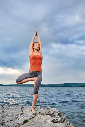 Young sporty woman doing different variants of yoga position on a rocky rivershore.