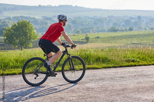 Young attractive cyclist riding mountain bike on the country road.