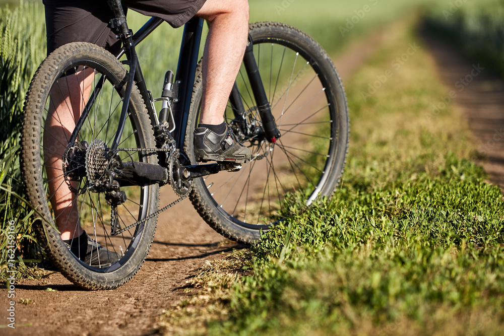 Closeup of cyclist man legs with mountain bike on outdoor trail in the summer field. Closeup of cyclist man legs with mountain bike on outdoor trail in the summer field.
