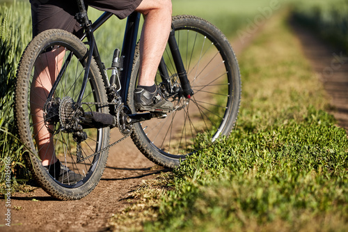 Closeup of cyclist man legs with mountain bike on outdoor trail in the summer field.