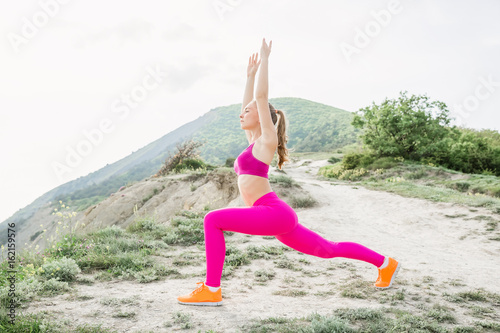 Young slim woman with perfect body is doing exercises at outdoor