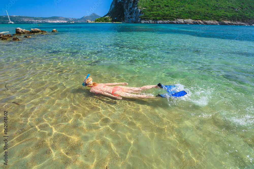 Young female in orange bikini snorkeling in beautiful clear waters of famous Voidokilia Beach in Peloponnese, Greece. Woman snorkeler swims in summer season. Water sports activities and leisure.