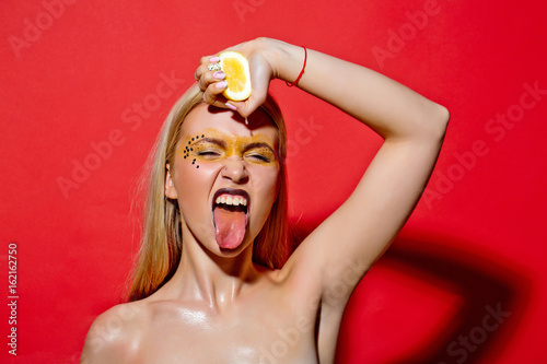 Billede på lærred young girl squeeze yellow lemon on red background