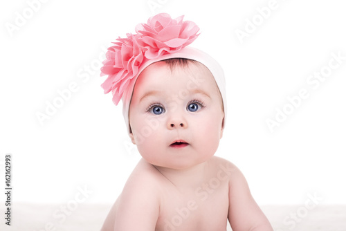 portrait of cute little baby girl with pink bow flower on her head, isolated on white. adorable child with big blue eyes looks into the camera
