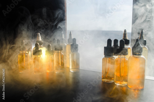 Vape concept. Smoke clouds and vape liquid bottles on window with sunlight on background. Light effects. Useful as background or vape advertisement or vape background. Close up