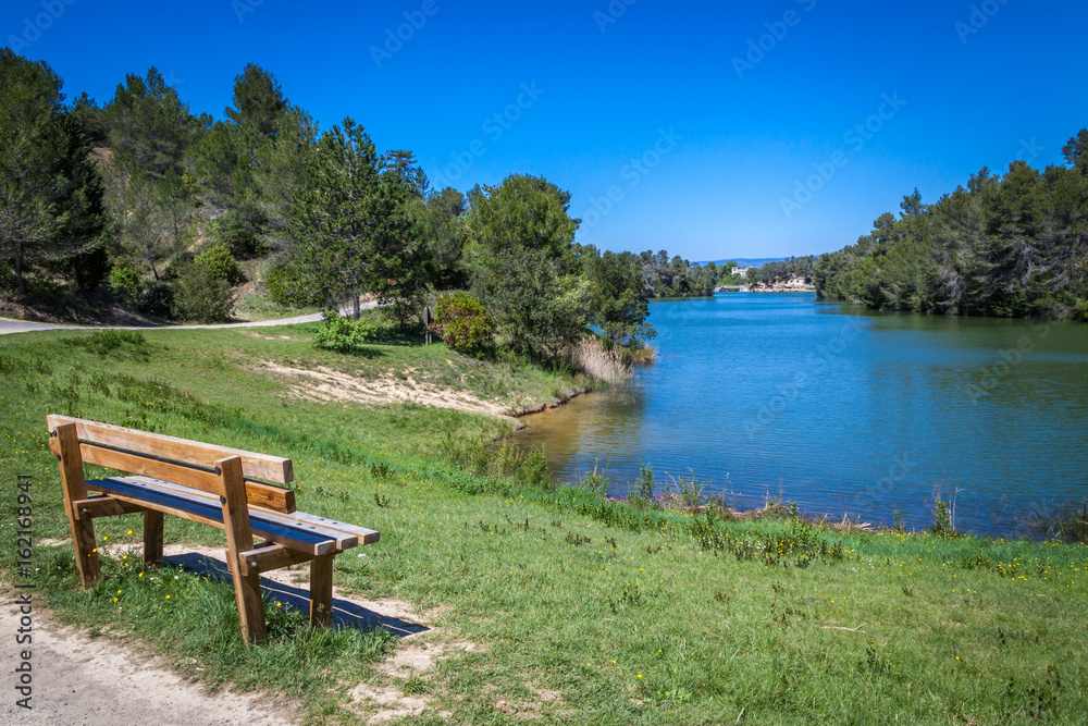 a view of blue Lac de Cavayere , artificial lake near Carcassone with green vegetation and a bench