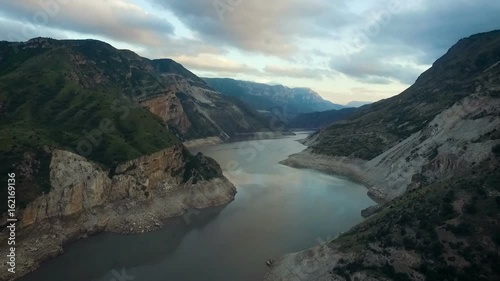 Caucasus Mountain River. Sunrise in Canyon. Cloudy Sky Reflecting on Water Surface. Rocky Hills. Green Slopes. Stone Bottom. Early Morning