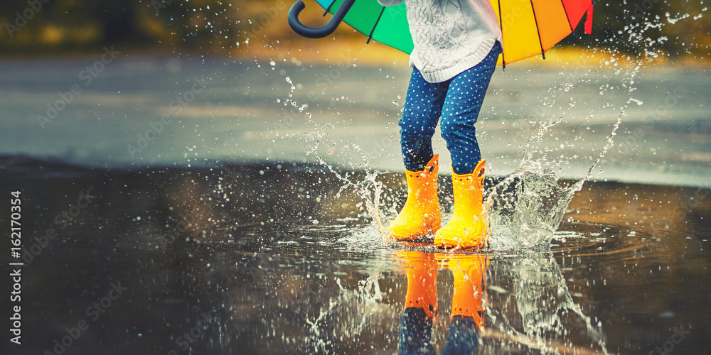 Fototapeta premium Stopy dziecka w żółtych kaloszach przeskakując kałużę w deszczu