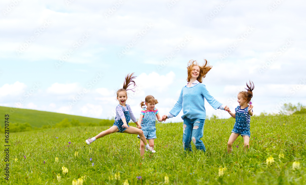 . Happy family mother and children daughter girls laughing and jump on   meadow in summer