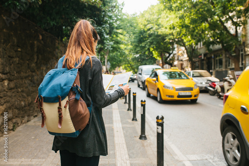 A young tourist girl with a backpack in a big city is watching a map. Journey. Sightseeing. Travel.