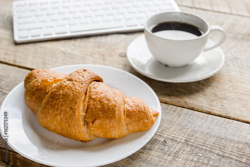 Businessman morning with keyboard, cup of coffee and croissant on wooden table background