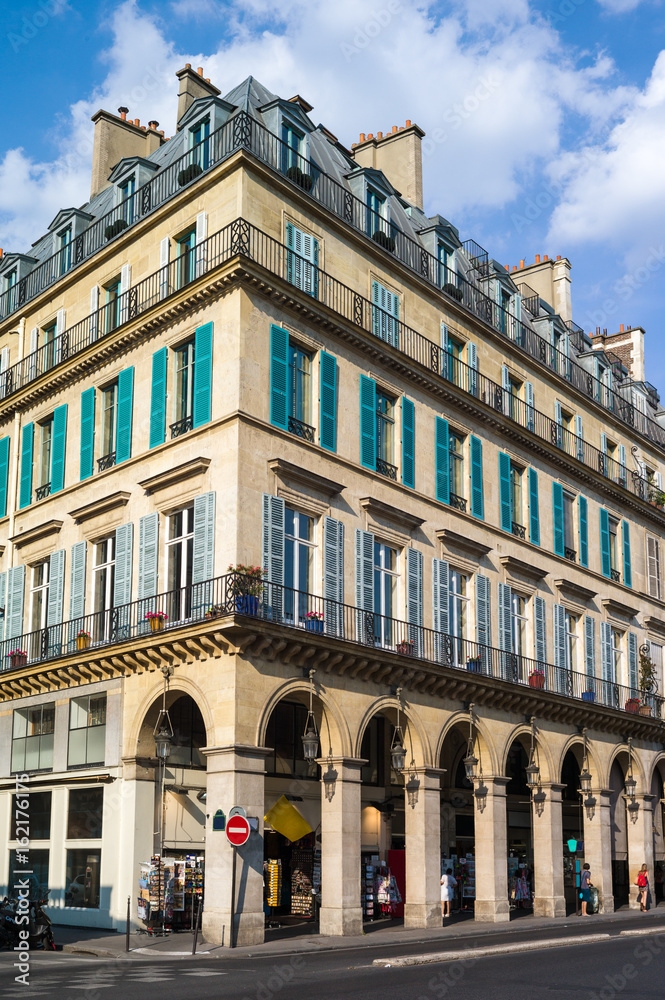 A typical Haussmannian building in Paris with balconies, shutters, arches and shops under a warm light of late afternoon.