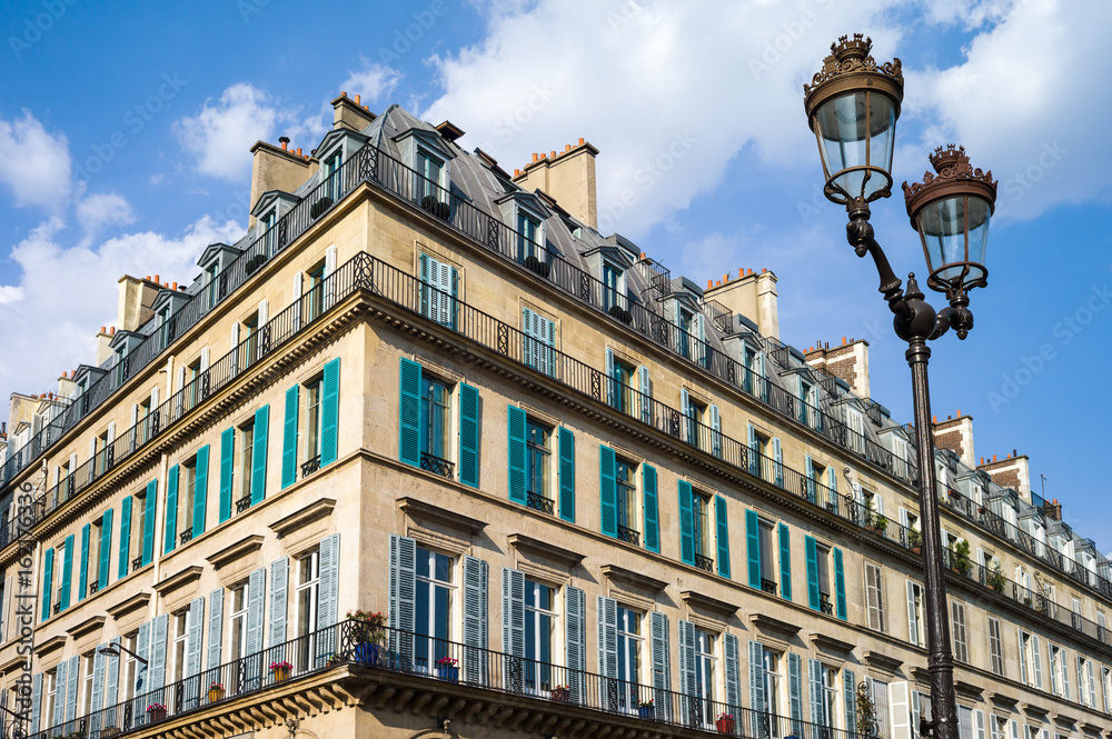 A typical Haussmannian building in Paris with balconies and shutters and a street light in the foreground under a warm light of late afternoon.