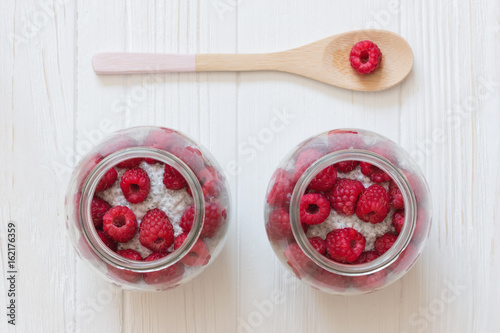 Glass jars of pudding from chia seeds with coconut milk and raspberry. Wooden spoon with berry in white wooden table. photo