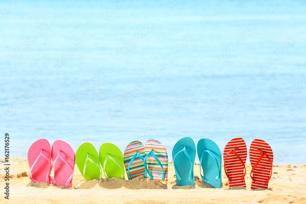 Naklejka premium Colorful flip-flops on sand at sea shore. Vacation concept
