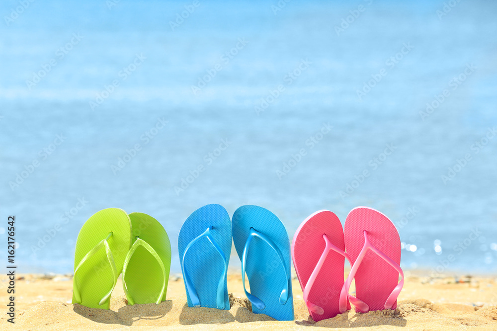 Fototapeta premium Colorful flip-flops on sand at sea shore. Vacation concept