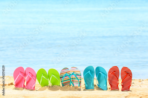 Colorful flip-flops on sand at sea shore. Vacation concept photo